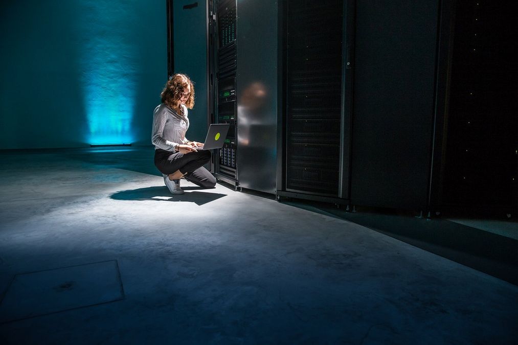 Photograph of an Arctur employee working on her laptop next to the super computer.