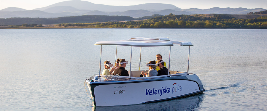 Five tourists wearing VR goggles and exploring in a small boat with a tour guide.