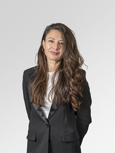 A portrait of Metka Špacapan, Head of WEB Department. She is a middle-aged woman with long brown hair, wearing a white shirt and a black jacket, smiling.