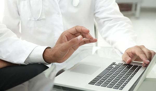 Photograph of two doctors during a meeting. One of them is pointing at the screen of a laptop in front of them.