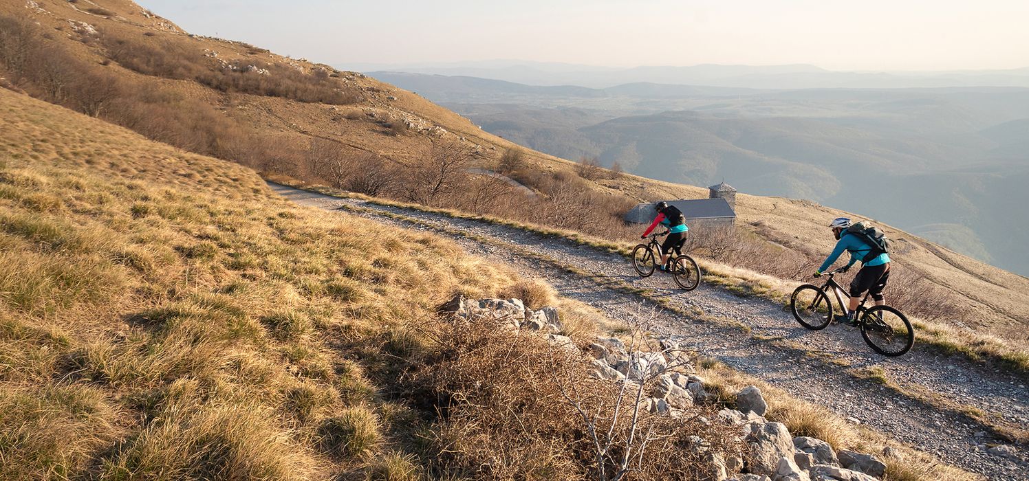 Two mountain bikers riding downhill overlooking a large valley.