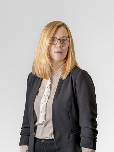 A portrait photograph of Martina Murovec, Chief Operating Officer. She is a middle-aged woman with long blonde hair and glasses, wearing a light grey shirt and a dark blue jacket, smiling.
