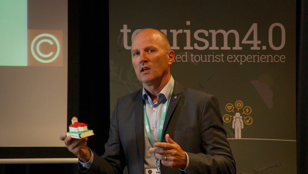 Photograph of Arctur CEO & Founder holding a model of a small church and talking with the audience. Behind him there is a poste titled tourism 4.0. 