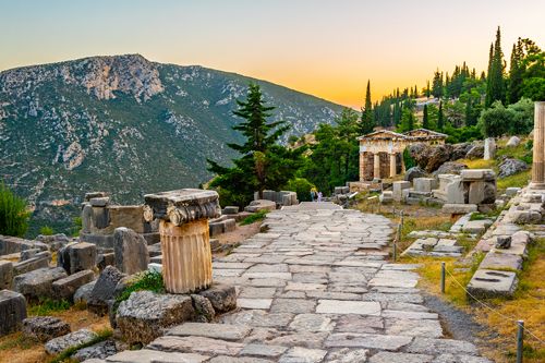 Sunset photograph of Ancient Greek ruins with a mountain in the background. 