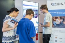 Photo of a woman and two boys looking at Reginna 4.0 fliers. In front of them is an interactive display screen.