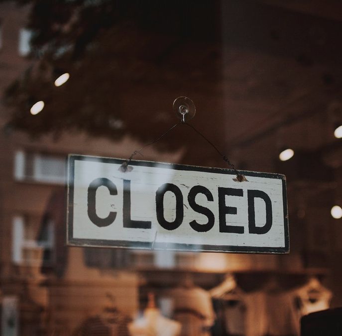 A close up photograph of a wooden sign titled "CLOSED" on a glass dor.