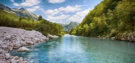 Soča river surrounded by a forest on both banks and mountains in the background.
