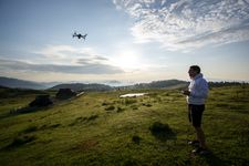 Photograph taken on Velika Planinan. It shows a drone operator operating a drone lifting an object next to a small church.