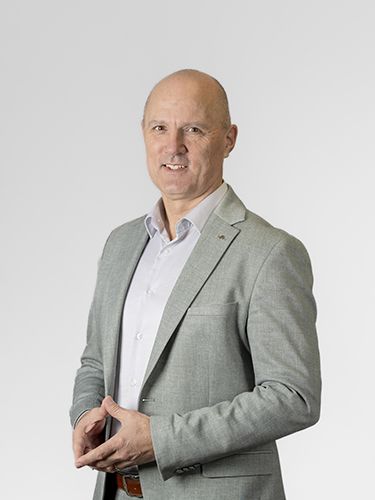 A portrait photograph of Tomi Ilijaš, Arctur's CEO & Founder. He is a smiling, middle-aged man with a clean-shaven head, wearing a light grey shirt and a grey jacket, smiling.