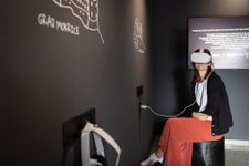 A woman sitting in a dark room wearing VR goggles and viewing a castle in the digital room e-Castles of Posavje.