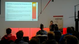 An Arctur employee is delivering a presentation titled 'AI-powered Next generation of VET' in front of the audience.