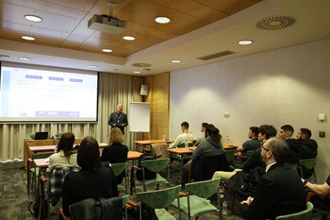 Photograph of a small crowd attending a lecture. The lecture is being projected on a screen.