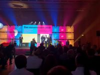 Day of innovation 2018 event. There are four people standing on a stage. Bellow the sage there is a photographer that is taking a picture of tree people on the stage holding nomination.
